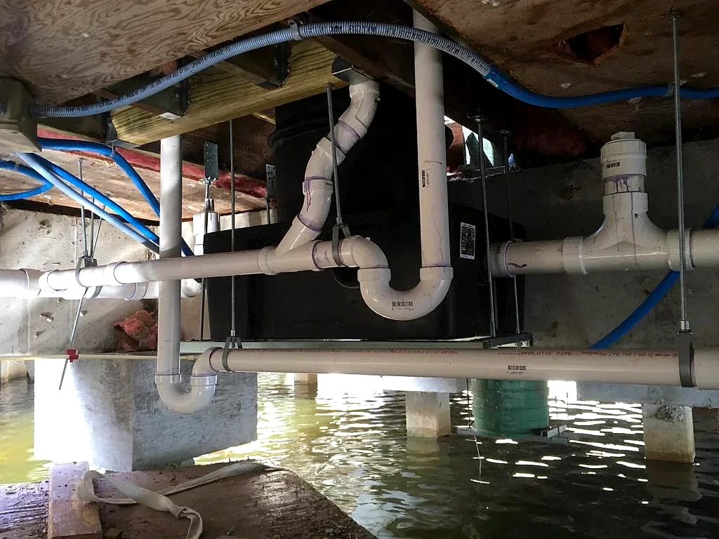 New PVC drain and waste lines hung under a raised waterfront home in South Florida